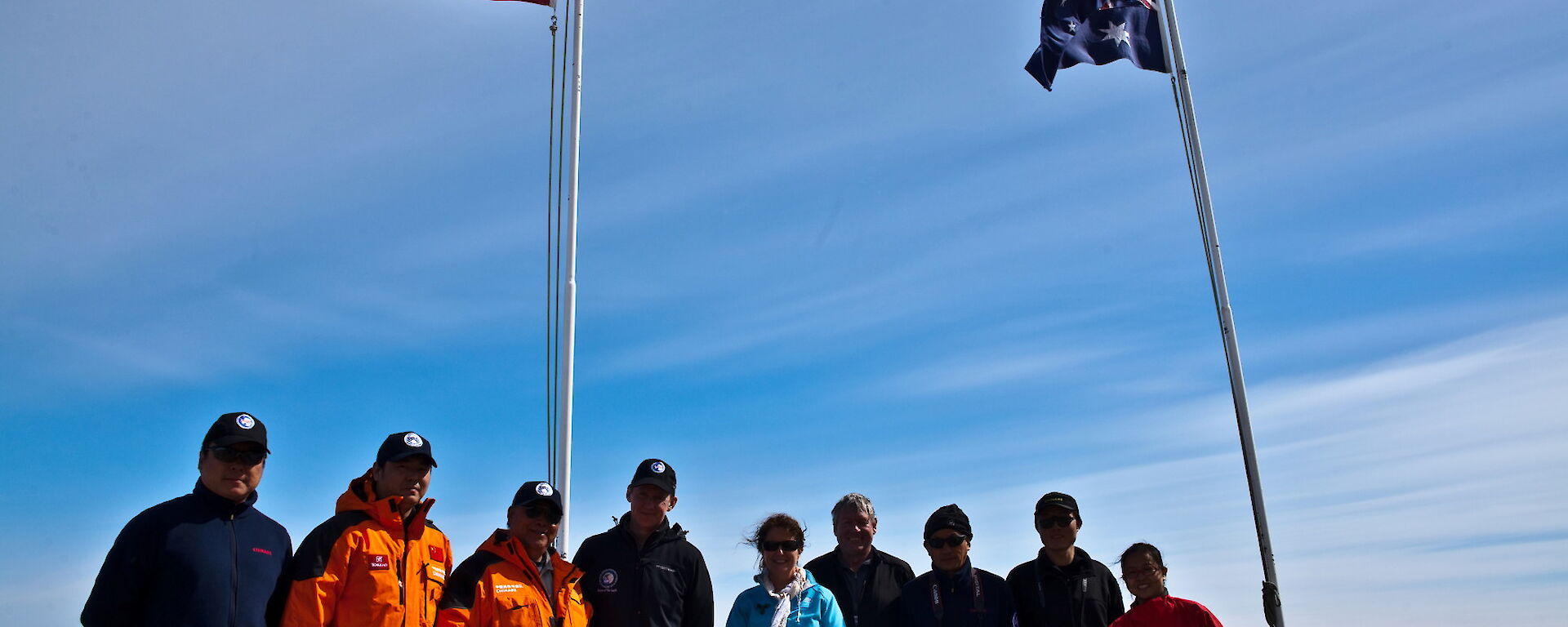 Chinese and Australian expeditioners standing together in foreground below national flags with Xue Long in background