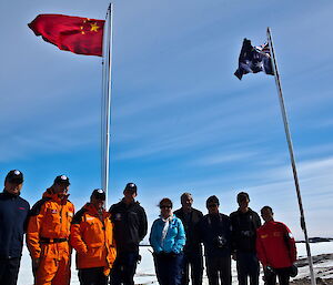 Chinese and Australian expeditioners standing together in foreground below national flags with Xue Long in background