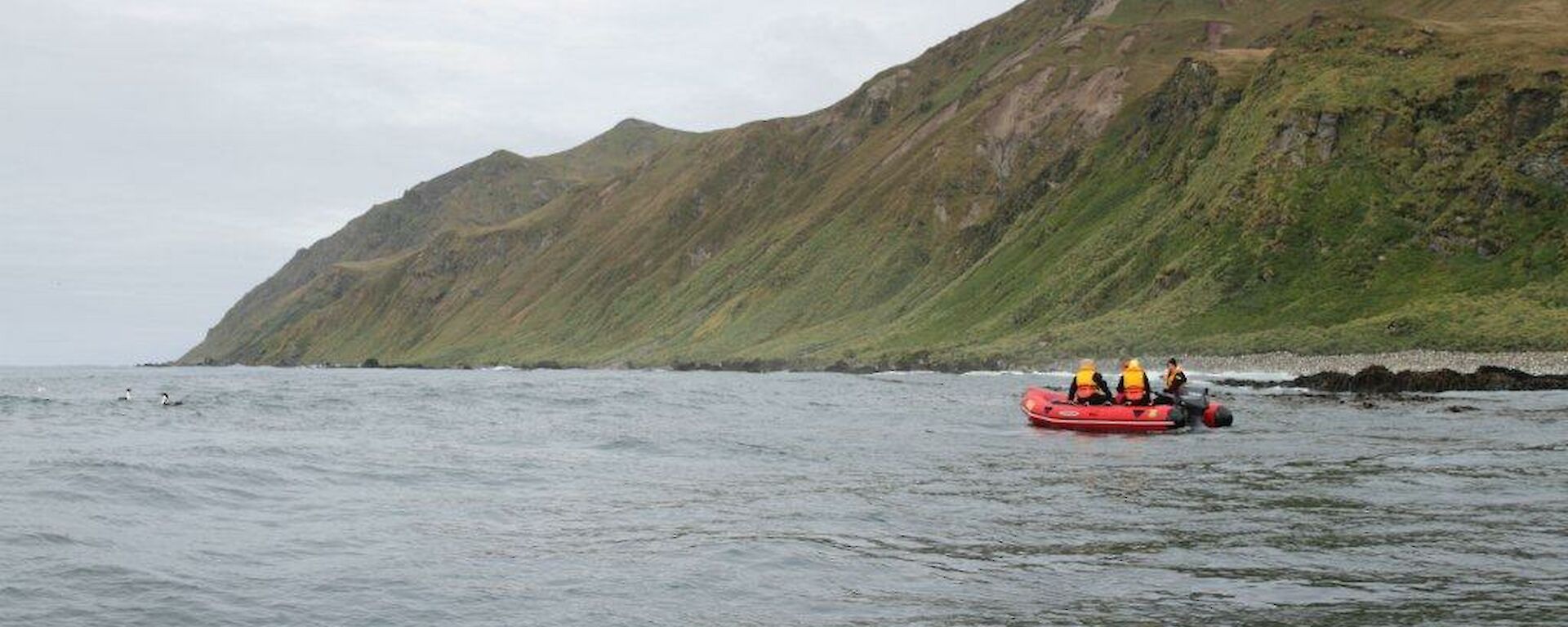 Long shot of orange boat on water with land in background