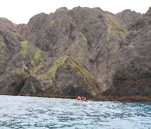 Expeditioners in a rubber boat dwarfed by the steep hills on shore