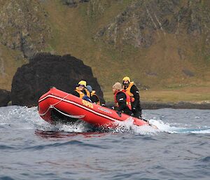 Four expeditioners in rubber boat heading away from the shore