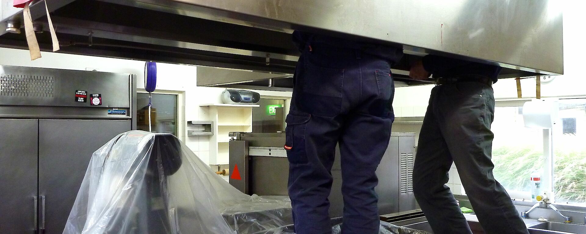 Legs of two men seen underneath industrial kitchen metal hood