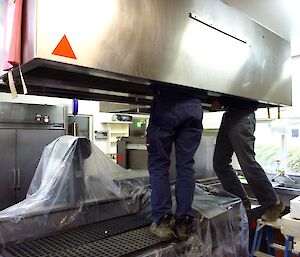 Legs of two men seen underneath industrial kitchen metal hood