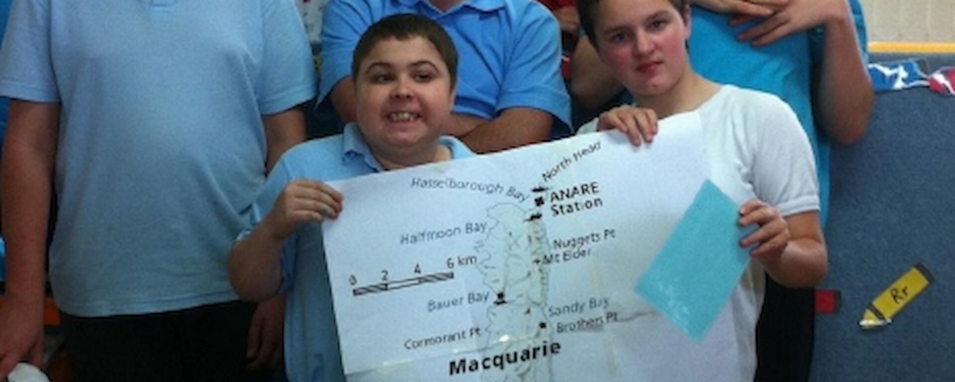 Five school students and their teacher hold a map of Macquarie Island.