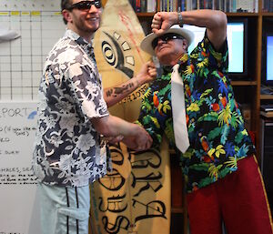 Richard and Jim pose in front of a surf board
