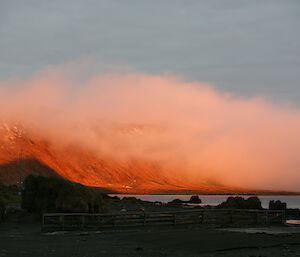 Sunrise over the west coast with orange mountain and cloud covering most of it to left of photo