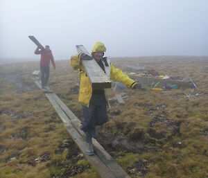 Andrew and Jim commence work on the boardwalk, carrying planks of wood on their shoulders