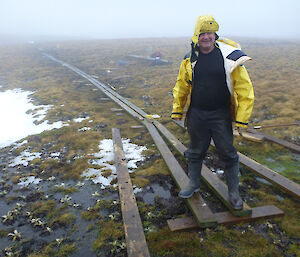Jim stands on wood planks outside on Macquarie Island, pausing from building boardwalk