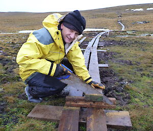 Mango joining in on the work, kneeling down over planks of wood on the ground