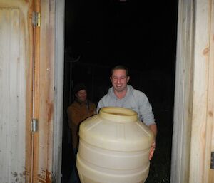 Andrew holds a large plastic brewery keg after cleaning it out, Tom in the background