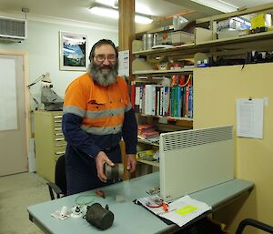 Ray, station electrician, pauses at his desk with an electrical motor he is about to check and repair