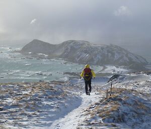 A yellow-clad AAD expeditioner heads towards station on a snowy, sunny day down the steep Doctor’s Track