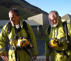 Two expeditioners dressed in yellow fire fighting equipment listening intentally