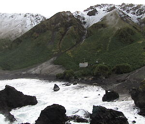 Looking across at a hut on the coast with large mountain slope in background