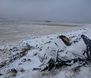 A snow-covered backpack sits on the ground surrounded by snow during an expeditioner’s lunch break