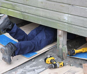 Tom’s legs and feet appear from under a building