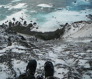 Expeditioner points camera at feet dangling over any icy cliff on Macquarie Island