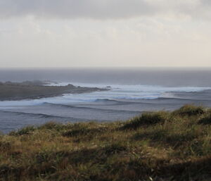 A view from grassy hillock of high waves cascading to shore