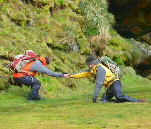 An expeditioner is helped out of wet ground on Macca