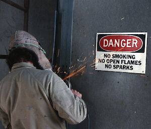 An expeditioner uses a power tool emitting sparks in front of a sign that says ‘Danger, no smoking, no open flames, no sparks'. Things were very different in 1984!