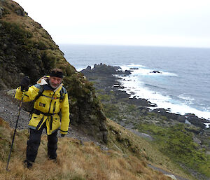 Gaz with hiking gear on a slight slope with sea and rocks on right