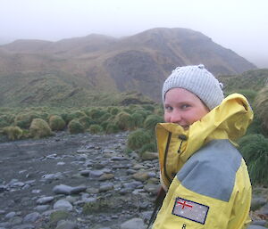 Karen poses on rocky beach with grass in background on Macquarie Island