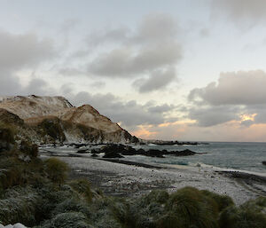 View from Green Gorge hut with cliffs on left and water on right, taken from grassy area near beach