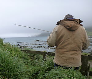 Charles relocating an air sparge with back facing camera, waist high in grass and ocean water before him