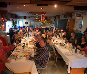 Expeditioners sit at two long tables and face the camera for a photo on Christmas day
