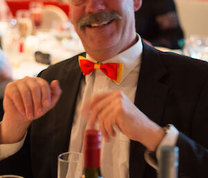 Greg seated at dinner with yellow and gold bow-tie and tuxedo shirt and jacket