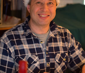 Charles sitting and eating at Christmas dinner, grins with Santa hat on that says “Merry Christmas” accross the front