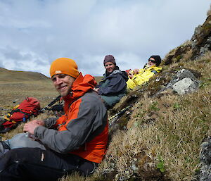3 expeditioners resting on a hill looking at the camera
