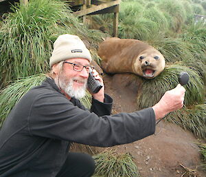 Expeditioner with a satelite phone talks to his partner back home holding speaker out to ele seal