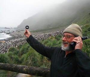 Expeditioner phoning home holds out phone to a large group of royal penguins