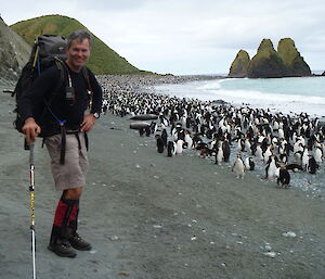 Male expeditioner standing alongside penguins on the beach