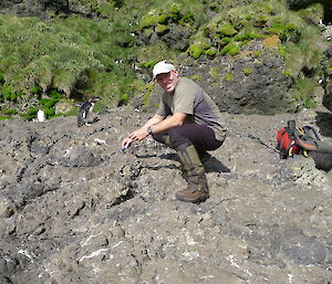 Expeditioner on rocks leaning over to pick up penguin scat