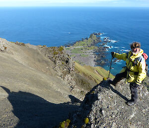 Expeditioner standing on a rocky ledge high up, ocean in background