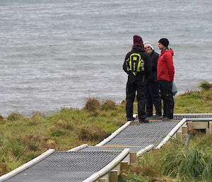 Three people on a boardwalk looking at views across to the ocean