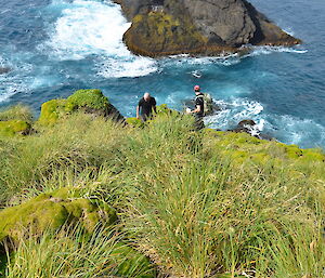 View looking down over a steep slope of two expeditioners, ocean in background