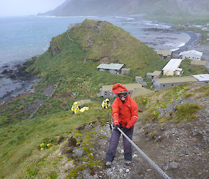 Eight expeditioners making their way up a steep hill with the use of a rope