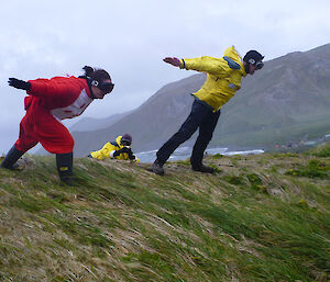 Two expeditioners leaning into very strong winds on a hill top
