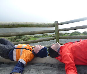 Two expeditioners lying on the ground heads together stretching