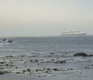 Two inflatable boats departing the beach heading towards a large white ocean cruiser