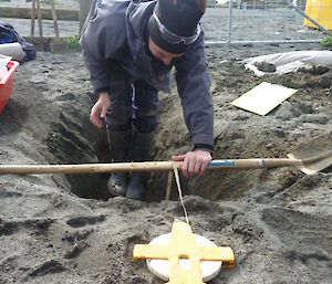 Expeditioner in a hole with a tape measure