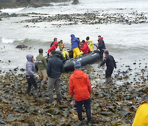 People in inflatable boats on the beach, lots of kelp on the beach