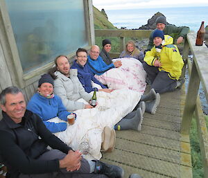 Expeditioners sitting with their backs against a wall high on a hill looking at the views and enjoying a few drinks