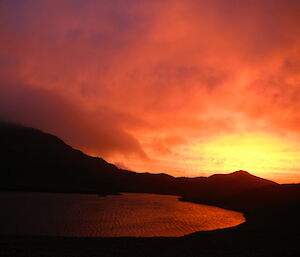 Bright orange and red sunset over a lake and hills