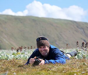 Expeditioner laying on the grass with his camera looking at the camera