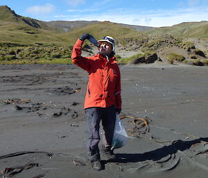 Expeditioner on the beach holding up a drink bottle