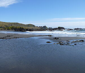 Photo of the beach, dark sand and ocean with the sun shining